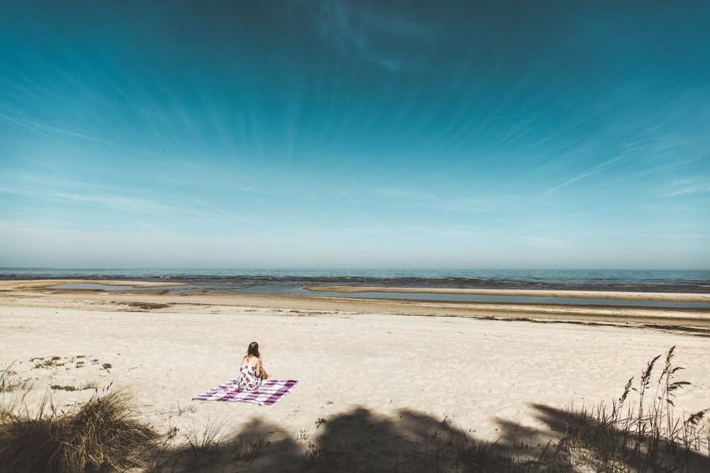 woman sitting on mat placed on gray sand during daytime