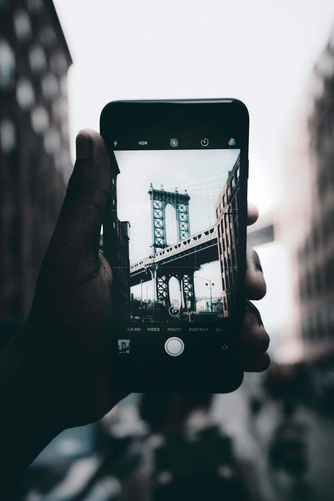 grayscale photography of person holding iPhone capturing bridge