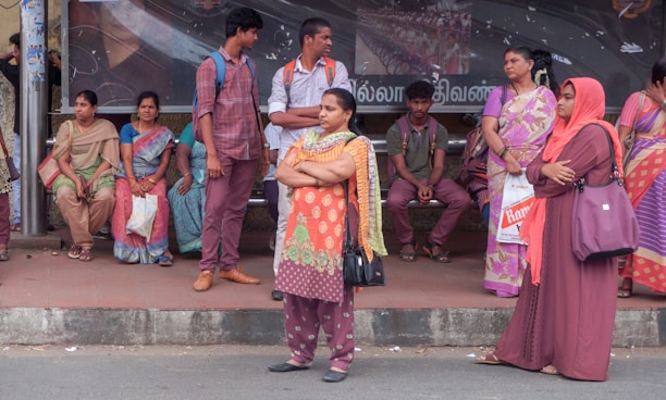 A diverse group of people smiling and chatting while waiting at a bus stop.