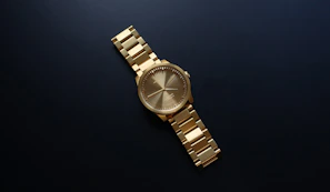 A minimalist black and gold watch set against a dark textured background.