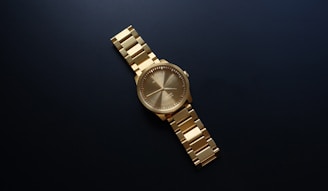 Close-up of a gold watch with a minimalist face against a dark velvet background.