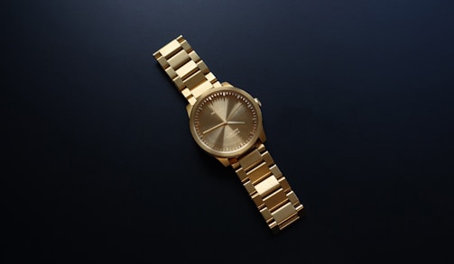 Close-up of a gold watch with a minimalist face against a dark velvet background.