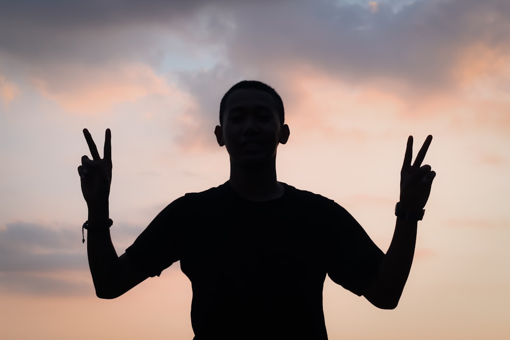 person doing peace hand sign with both hands silhouette