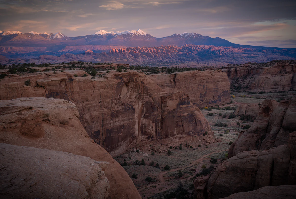 A sandstone canyon near Moab at dusk, below snowy mountains