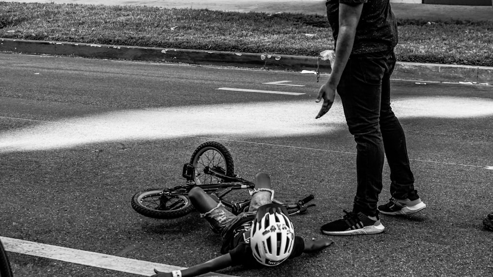 criança deitada no chão ao lado da bicicleta e homem em pé