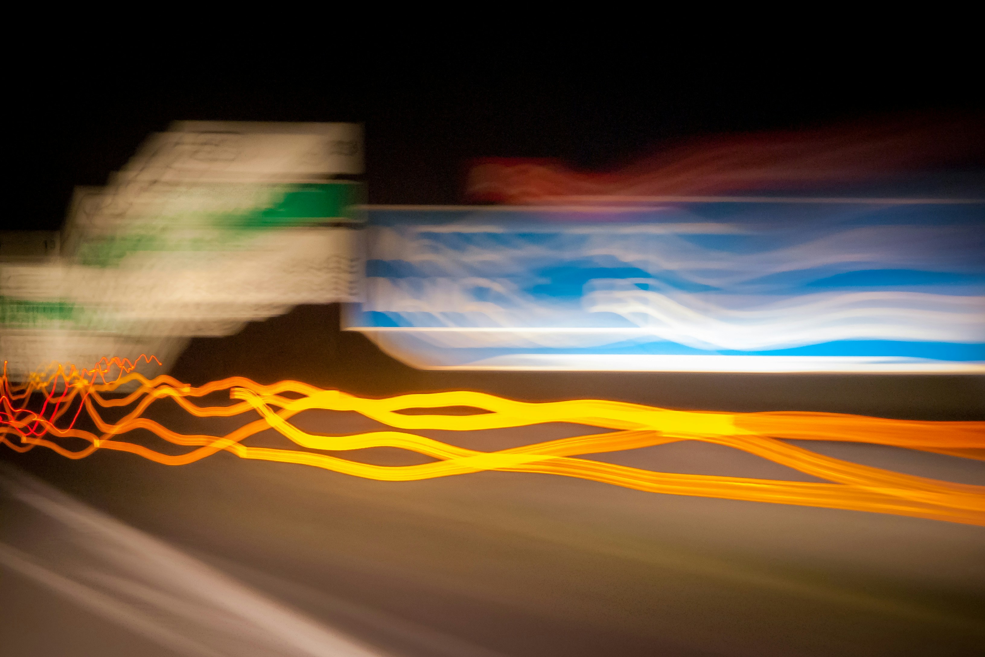 Bored on the passenger seat in the middle of the night on a highway in France ;) I like to drive, but sometimes you just need to have a rest and while my partner was driving I had some time to play with my camera. For this shot I (tried to) focus on a blue and white motorway sign and tried to “follow” that sign while we drove past it. Can’t really remember the orange/red lights; it wasn’t traffic, I guess it was because of road works :)