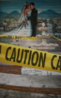 A mural depicting a bride and groom in a wedding scene with a landscape background is visible. In front of the mural, there is yellow caution tape with the word 'CAUTION' written on it.
