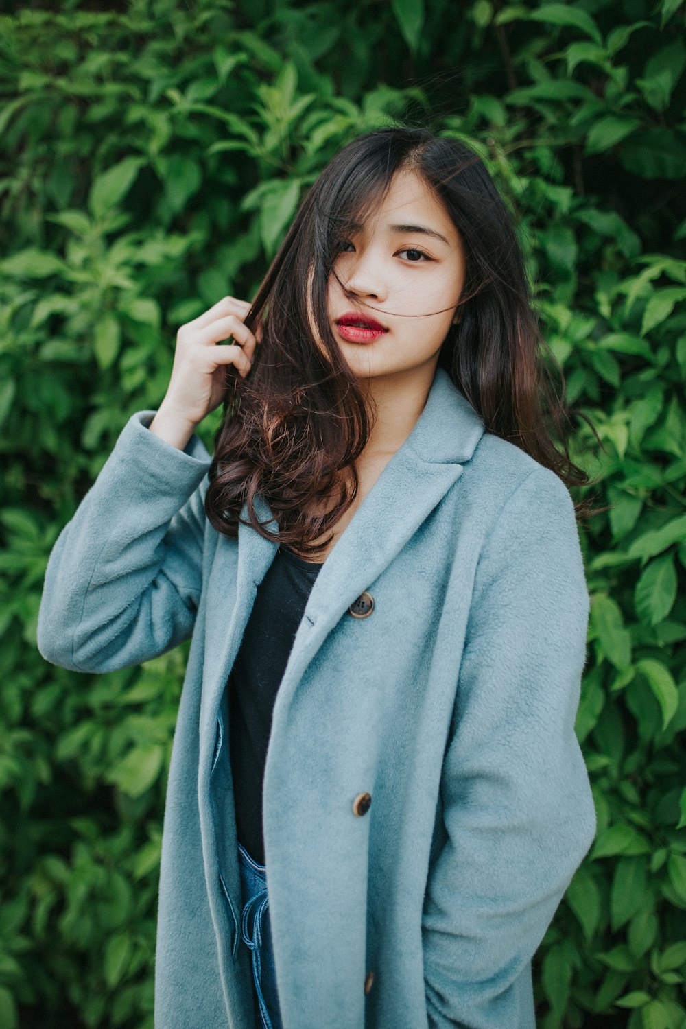 femme en manteau gris debout près des plantes vertes