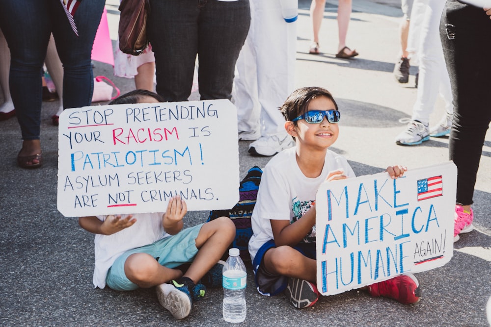 two children sits on ground holding placards