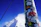 Close-up of a Send Stick attached to a ski with a cold can, snow-covered peaks in the background.