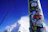 Close-up of a Send Stick attached to a ski with a cold can, snow-covered peaks in the background.