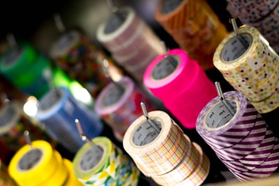 Several rolls of colorful decorative tape are neatly arranged in rows, each with a unique pattern and vivid colors. The tapes are mounted on metal rods, creating an appealing display that highlights the variety in design.