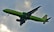 A green commercial airplane with the logo S7 on its body and tail is flying against a cloudy sky. The aircraft is in mid-flight with its landing gear extended, indicating either a landing or takeoff phase.