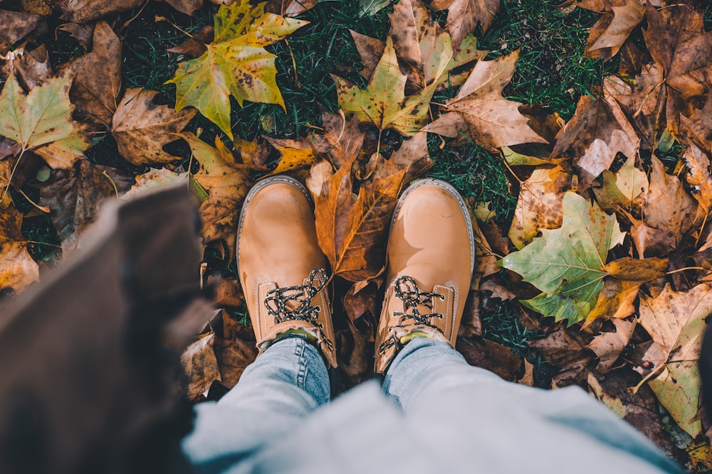person in brown leather boots standing in ground surrounded with leaves