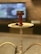 A hookah with a red bowl and burning coals sits on a white tray. The background features a blurred television screen and a brick wall, creating a cozy and relaxed ambiance.