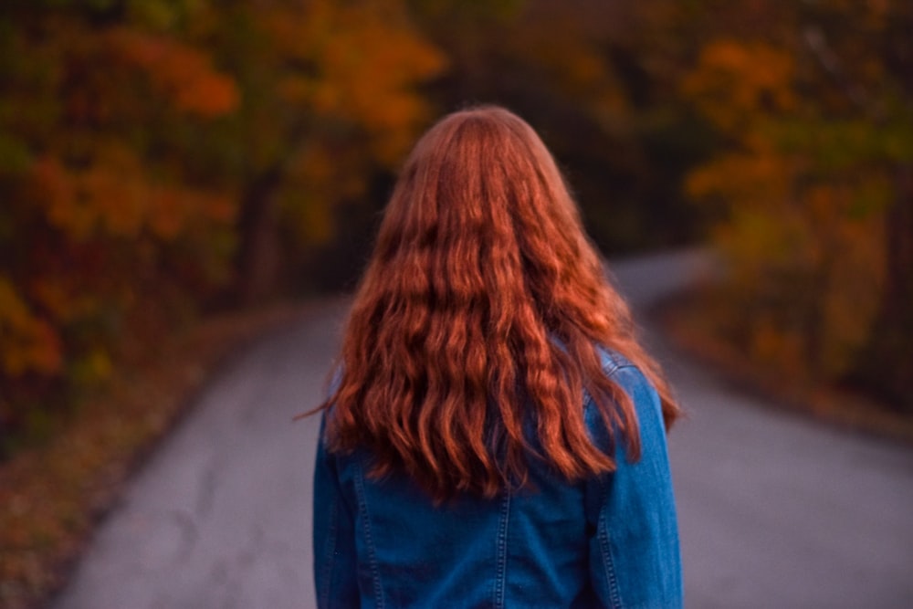 woman in denim jacket walking on empty road