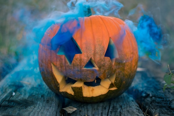A carved pumpkin with blue smoke coming out of it.