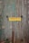 A weathered wooden door with peeling aquamarine paint, featuring a yellow sign with red text written in Greek. A terracotta pot with a small plant can be seen at the bottom left corner.