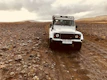 A rugged off-road vehicle climbing a rocky hill with dusty terrain