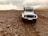 A rugged white off-road vehicle is traveling on a rocky terrain under an overcast sky. The landscape is barren with scattered rocks and minimal vegetation, set against a backdrop of distant hills.