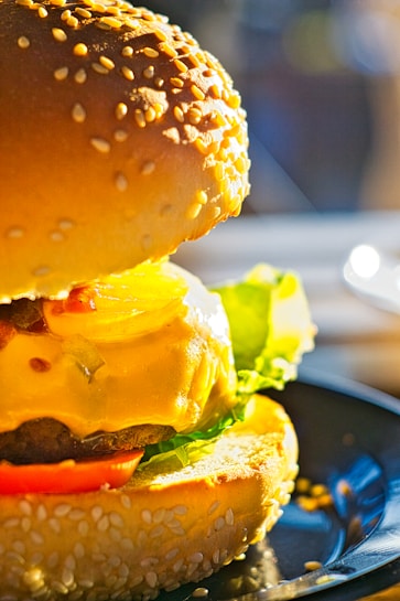 A close-up view of a delicious cheeseburger with a sesame seed bun. The burger is topped with melted cheese, fresh lettuce, and a slice of tomato. The lighting highlights the textures of the bun and cheese, creating a mouth-watering appeal.