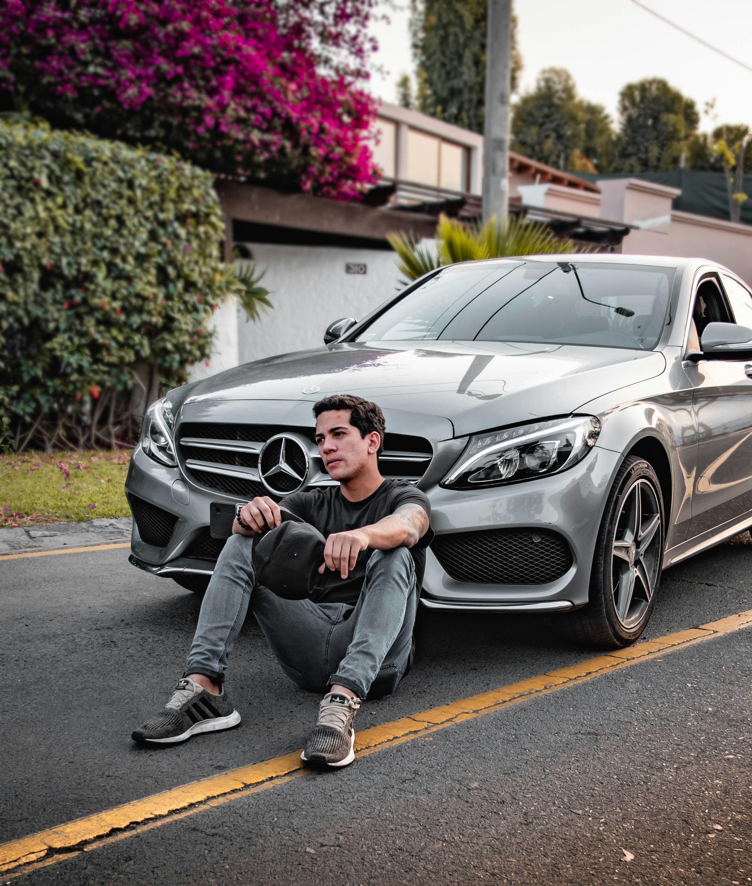 Man sitting beside silver Mercedes-Benz car outdoors