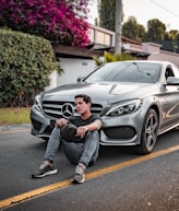 unknown celebrity sitting siting beside silver Mercedes-Benz car outdoors