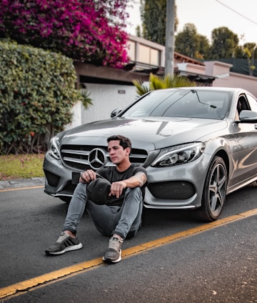unknown celebrity sitting siting beside silver Mercedes-Benz car outdoors