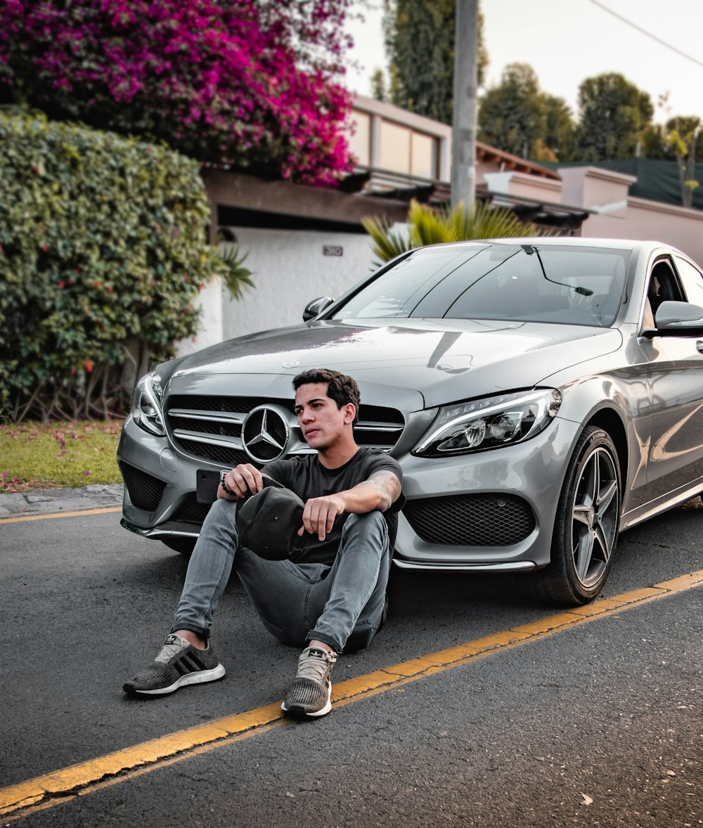 celebridad desconocida sentada sentada al lado del coche plateado de Mercedes-Benz al aire libre