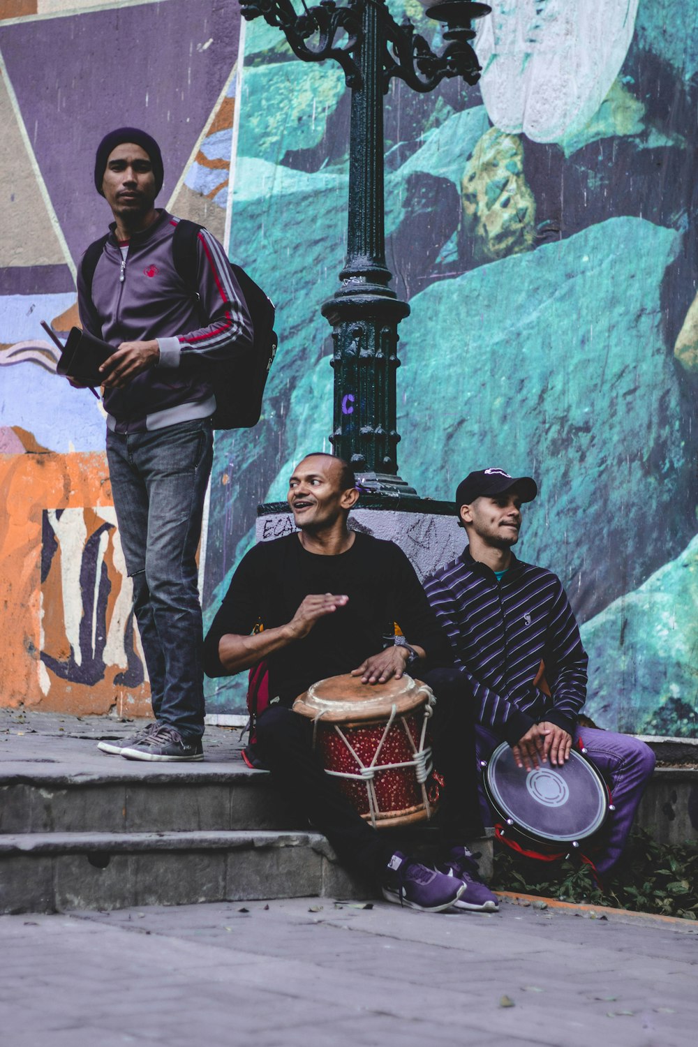 three men sitting beside black street lamp