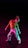 A dancer poses with a dynamic stance against a dark background, illuminated by colorful lights that cast hues of red and green. The dancer wears a bright yellow top and white pants, creating a vivid contrast with the darkness.