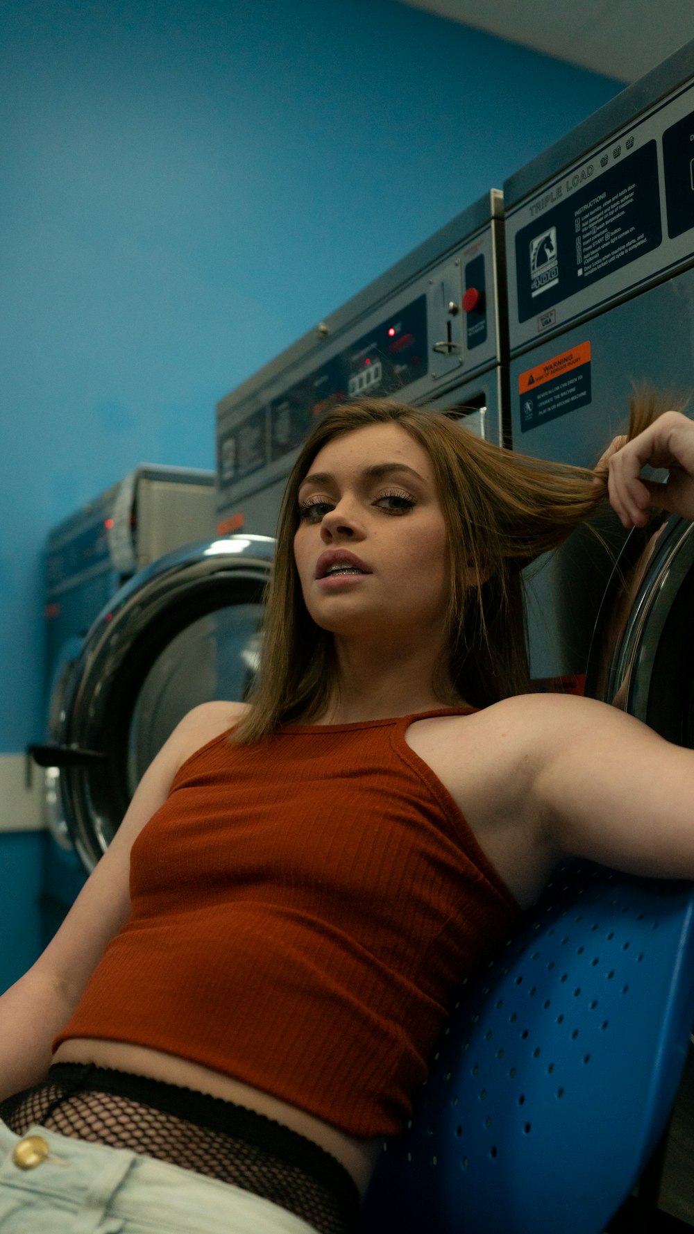 Mujer sentada sosteniendo su cabello cerca de la lavadora en la lavandería