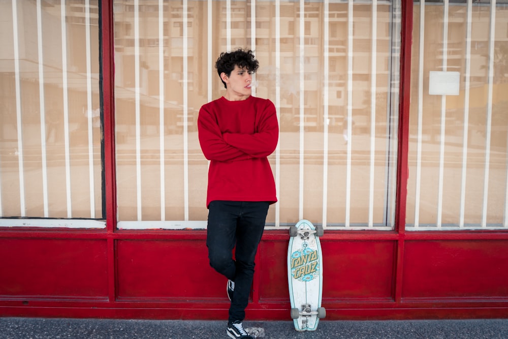 man leaning on glass wall beside leaning skateboard