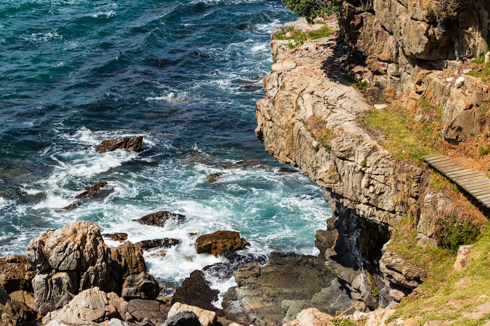 water waves hitting rocks under hill at daytime