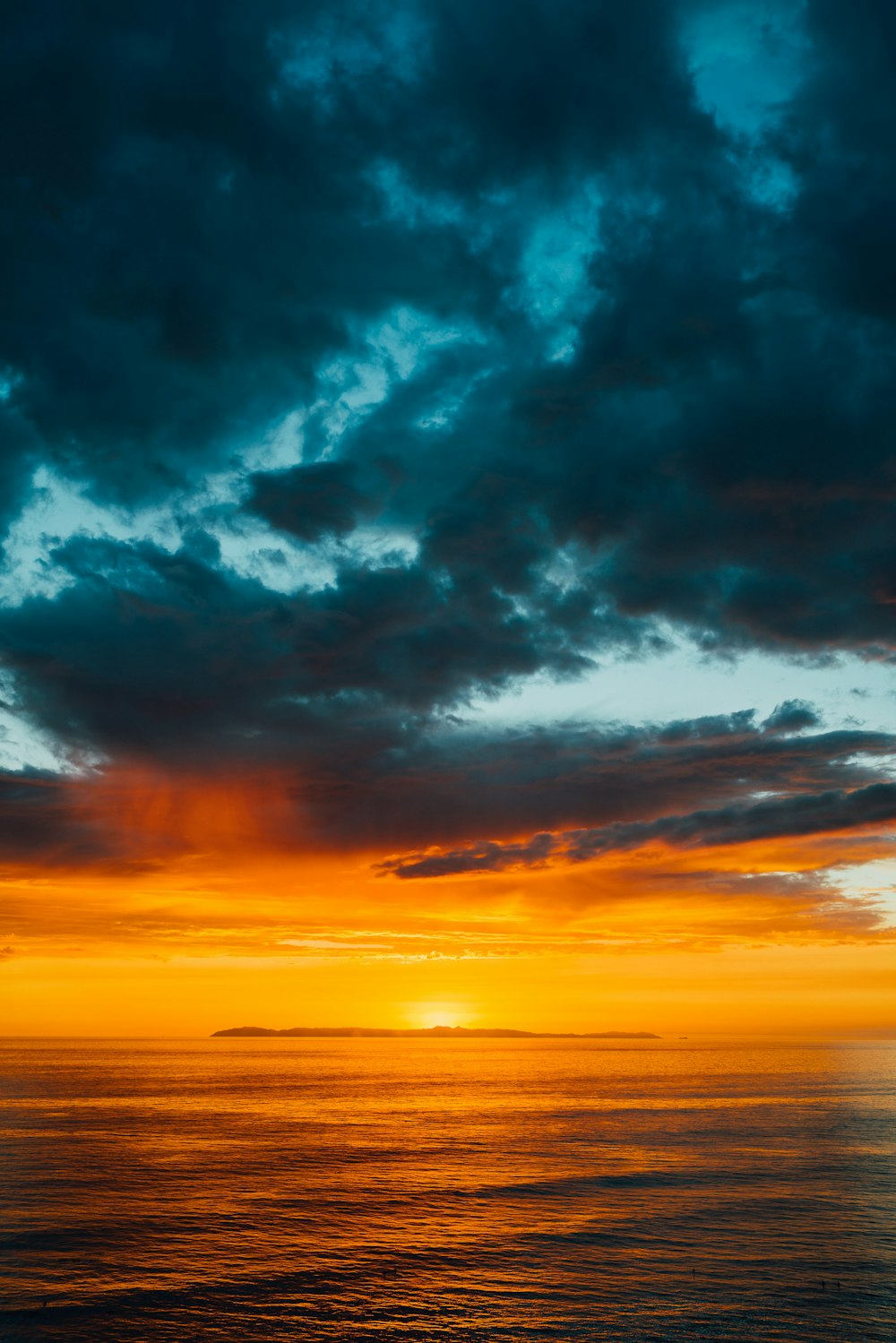 夕暮れ時の海のオレンジ色の空を部分的に覆う緑と黒の雲