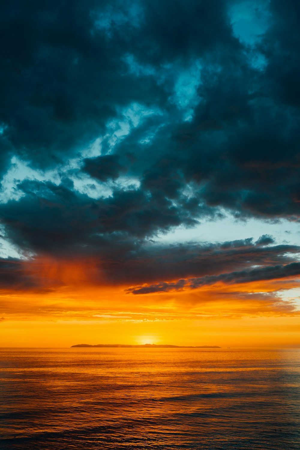 Grüne und schwarze Wolken bedecken teilweise den orangefarbenen Himmel über dem Meer bei Sonnenuntergang