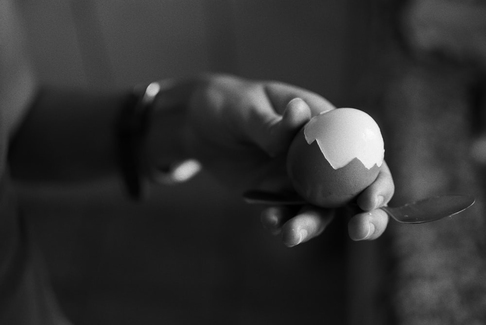 gray scale photo of person holding boiled egg
