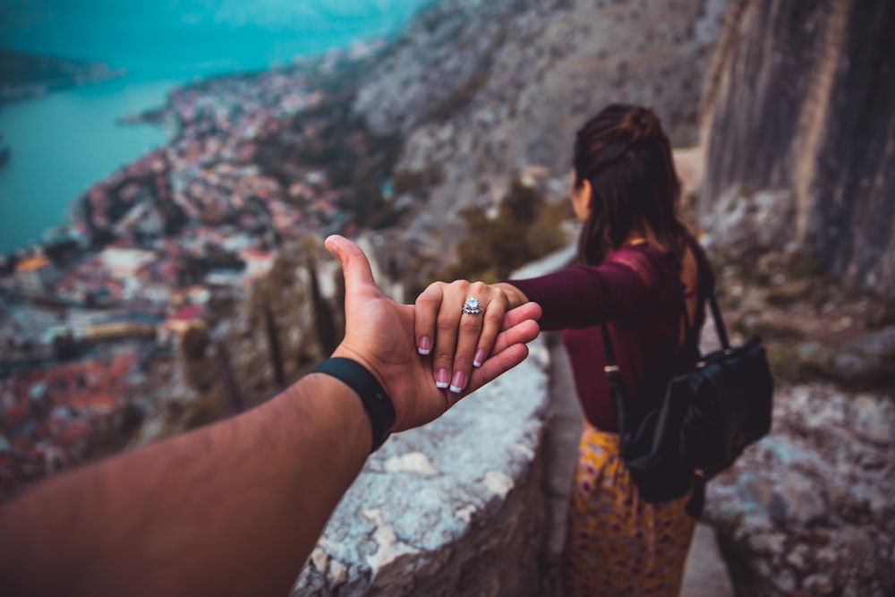 femme tenant la main de l’homme tout en regardant le paysage d’un bâtiment à côté d’un plan d’eau pendant la journée