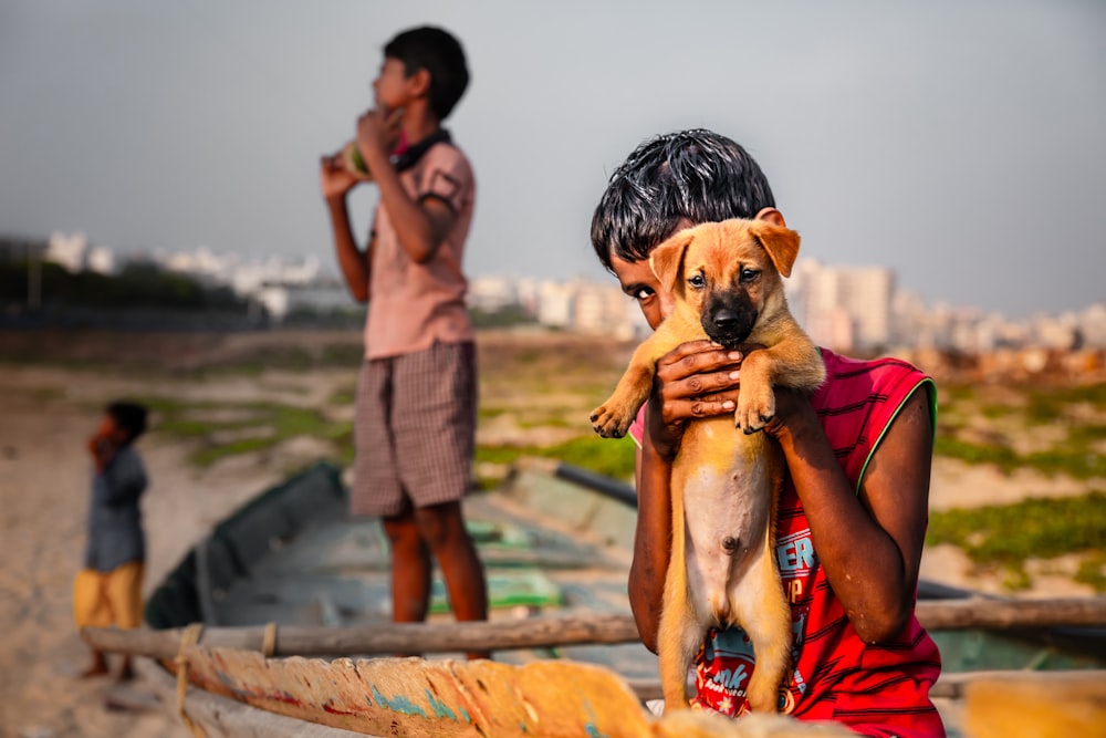 boy in red sleeveless shirt holding brown short-coated puppy