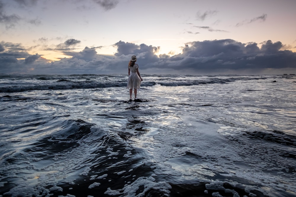 Frau, die während des Sonnenaufgangs am Meeresufer steht