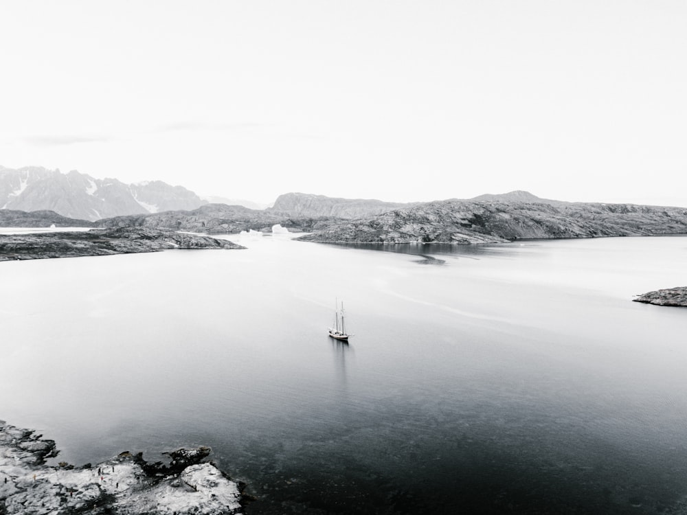 Fotografía en escala de grises de un barco cerca de la montaña