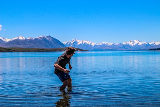 man throwing pebble on ocean water in Lake Tekapo New Zealand