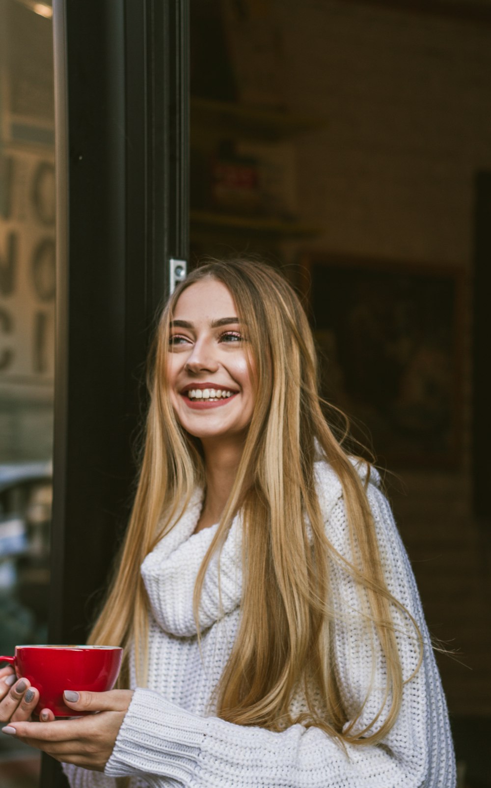 smiling woman wearing white sweater while holding cup