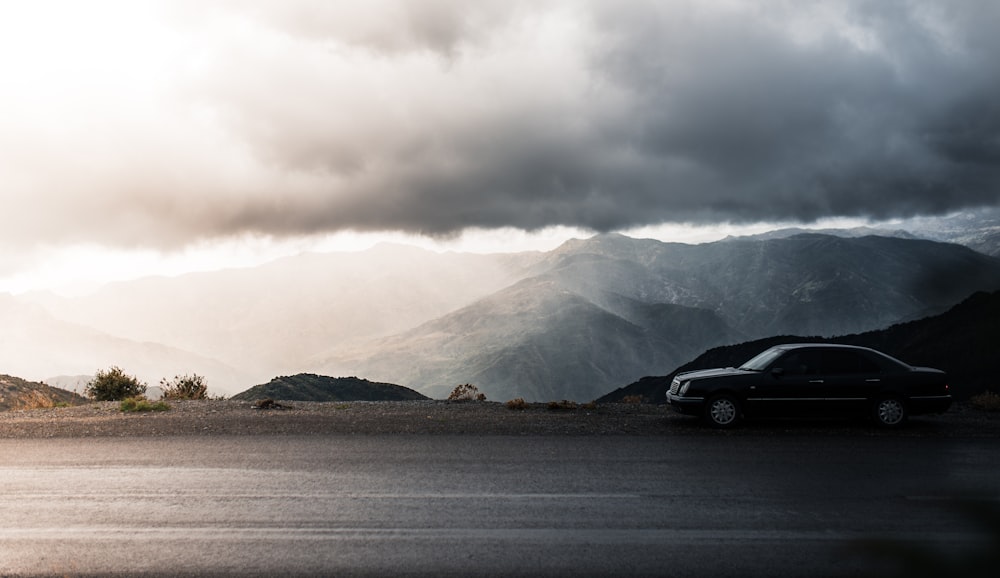 black sedan parked beside road near mountain during daytime