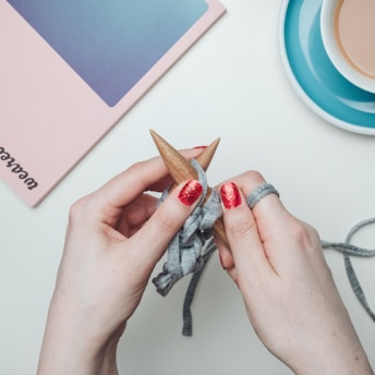 person holding two brown knitting tools