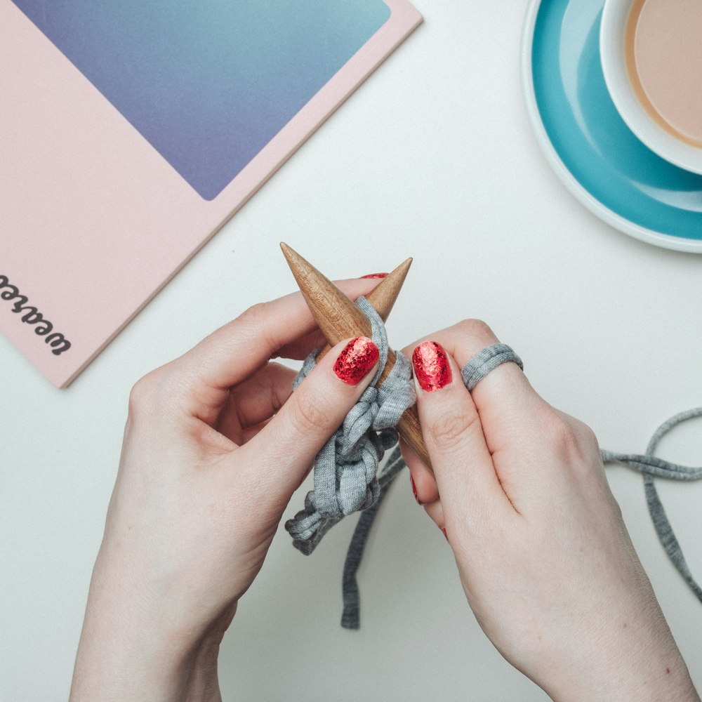 person holding two brown knitting tools