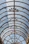 A glass roof with an intricate metal framework featuring circular and geometric designs. Sunlight filters through, creating a pattern of shadows and light on the surface.