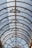 A glass roof with an intricate metal framework featuring circular and geometric designs. Sunlight filters through, creating a pattern of shadows and light on the surface.