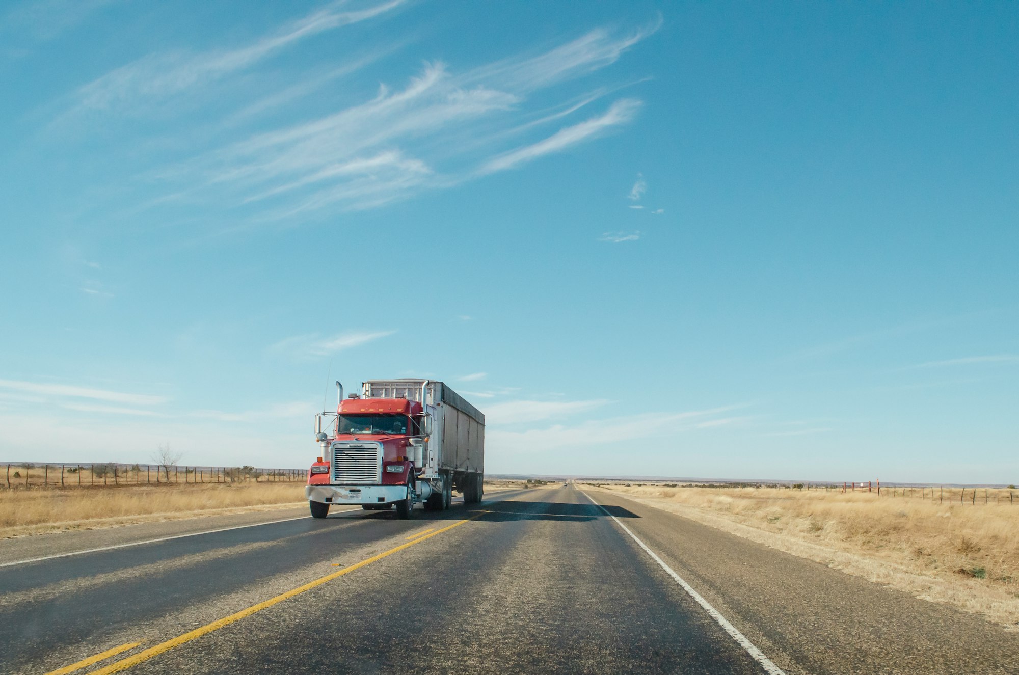 A red semi truck driving along a West Texas road