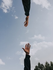 Ištiestos rankos melsvame danguje, simbolizuojančios pagalbą, susisiekimą ir psichoterapijos konsult